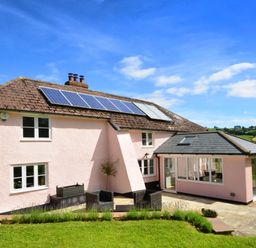 A two story house with solar panels on the roof and outdoor seating on a patio at Culverwells in Axminster