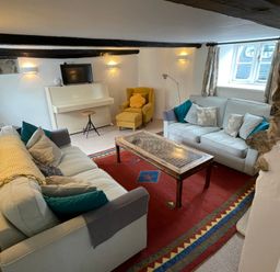 A living room with two sofas a yellow armchair a piano and a red patterned rug at Culverwells in Axminster