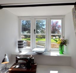 A window with a stack of bowls a sewing machine a plate and a vase with flowers at Culverwells in Axminster