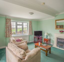 A living room with two couches, a wooden coffee table, TV on a stand, a fireplace with a mirror above it, and floral curtains at The Doves in Burton Bradstock