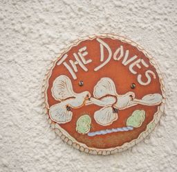 A circular ceramic sign with two doves and the words The Doves on a textured white wall at The Doves in Burton Bradstock