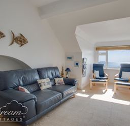 A living room with a blue leather sofa, two blue armchairs, a window with a sea view, and wall decorations at Dream View in Greenhill