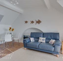 A living room with a blue sofa and nautical cushions next to a glass dining table with white chairs and sunflowers at Dream View in Greenhill