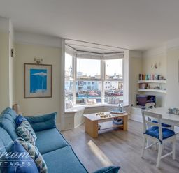 A living room with blue sofa white dining table with blue cushions and a bay window with a seating area at Harbour Edge in Brewers Quay Harbour