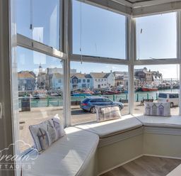 A bay window seating area with cushions overlooking a street and waterfront at Harbour Edge in Brewers Quay Harbour