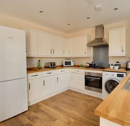 A kitchen with white cabinets wooden countertops a fridge oven microwave washing machine and a sink at The Ferns in Weymouth