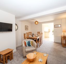 A living room with a mounted television a dining table with chairs and a wooden coffee table at Firkin Cottage Brewers Quay Harbour