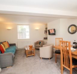 A living room with a gray sofa with colorful cushions two beige armchairs a wooden coffee table and a wooden dining table with four chairs at Firkin Cottage in Brewers Quay Harbour