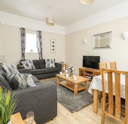 A living room with gray sofas a wooden coffee table a TV on a wooden stand and a dining table with wooden chairs at Footprint in Brewers Quay Harbour