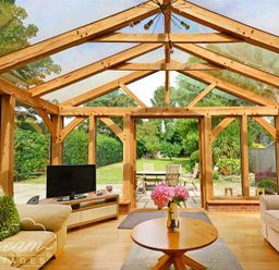 A sunroom with wooden beams glass walls a television on a stand and sofas around a wooden coffee table with flowers at Fossil Barn in Weymouth