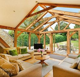 A living room with beige sofas and a round wooden table under a wooden frame glass ceiling at Fossil Barn in Weymouth