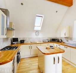 A kitchen with wooden countertops white cabinets an island a gas stove a microwave and a skylight at Fossil Barn in Weymouth