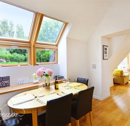 A dining area with a wooden table set for four under skylight windows and a living room visible through an arch at Fossil Barn in Weymouth
