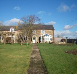 A stone house with a pathway leading to the door and a garden with trees and grass at Grazeland Cottage in Bridport