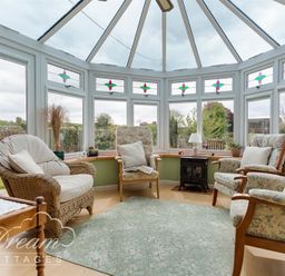 A conservatory with armchairs a wicker chair a small stove and plants at Grazeland Cottage in Bridport