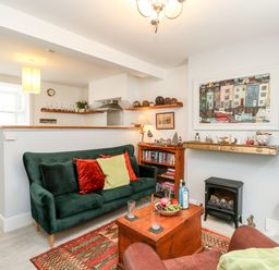 A living room with a green sofa, wooden coffee table, shelves with books and decorations, and a painting above a small stove at Harbour Catch Cottage in Weymouth