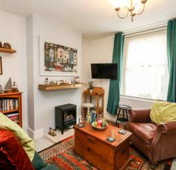 A living room with a leather armchair green curtains a wooden chest as a coffee table and a wall mounted tv at Harbour Catch Cottage in Weymouth