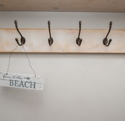 A wooden coat rack with six metal hooks and a sign hanging that reads gone to the beach at Harbourside House Brewers Quay Harbour