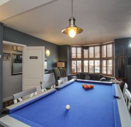 A game room with a blue pool table chairs a sofa striped armchair and windows with shutters at Harbourside House in Brewers Quay Harbour