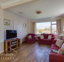 A living room with red sofas a wooden TV stand and a large window at Hillview Bungalow in Burton Bradstock