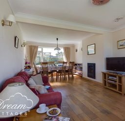 A living room with a red sofa a wooden dining table and chairs a television and a fireplace at Hillview Bungalow in Burton Bradstock