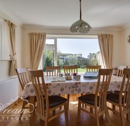 A dining room with a table and eight chairs by a window and sliding glass door at Hillview Bungalow Burton Bradstock
