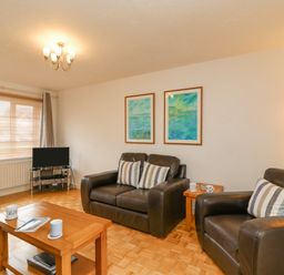 A living room with two framed paintings on the wall a wooden coffee table with mugs and a magazine brown leather sofas a small television and a beige armchair at Home Waters in Wyke Regis