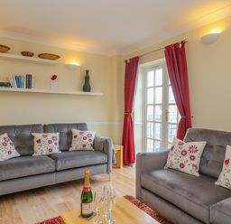 A living room with two gray sofas with floral pillows a wooden coffee table with a bottle and glasses and shelves on the wall at Hops House in Brewers Quay Harbour