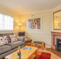A living room with a gray sofa and patterned cushions a wooden coffee table with a bottle and glasses a fireplace and a colorful painting on the wall at Hops House in Brewers Quay Harbour