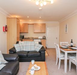 A living room with black sofas and a dining table with chairs next to a kitchen area at Harbour Watch Apartment 1 Brewers Quay Harbour