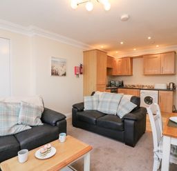 A living room with two black sofas and checkered cushions next to a kitchen with wooden cabinets and a dining table at Harbour Watch Apartment 1 Brewers Quay Harbour