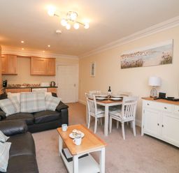 An open plan living and dining area with two black leather sofas and a wooden coffee table with cups and cupcakes at Harbour Watch Apartment 1 Brewers Quay Harbour