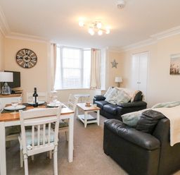 A living room with two black sofas a dining table set with plates and glasses and a wall clock at Harbour Watch Apartment 1 in Brewers Quay Harbour
