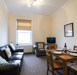 A living room with a black leather sofa, armchair, dining table set with plates and glasses, and a television at Harbour Watch Apartment 6 Brewers Quay Harbour