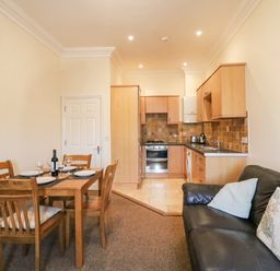 A kitchen and dining area with wooden table and chairs next to a black sofa at Harbour Watch Apartment 6 Brewers Quay Harbour