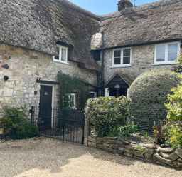 A stone cottage with a thatched roof and a garden at Ivy Cottage in West Lulworth