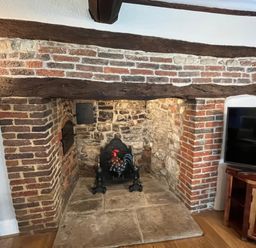 A fireplace with a wooden beam and stone wall at Ivy Cottage in West Lulworth