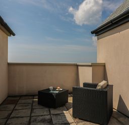 An outdoor patio with a black wicker armchair with cushion and a matching table with a cup and pastry at Jurassic Coast House in Portland