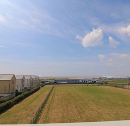 A large fenced grassy field with rows of houses on the left and industrial buildings in the distance at Jurassic Coast House in Portland
