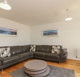 A living room with a gray sectional sofa and patterned pillows a round coffee table and framed pictures on walls at Jurassic Coast House in Portland