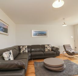 A living room with a sectional leather sofa chairs round coffee table and framed pictures on the wall at Jurassic Coast House in Portland