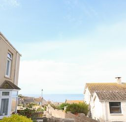 A view of houses and a garden wall overlooking the sea under a blue sky at Langham Cottage in Portland