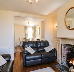 A living room with leather sofas and a fireplace opening to a dining area with a table and chairs at Langham Cottage Portland