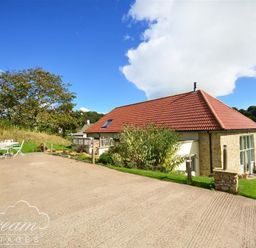 A stone cottage with a red tiled roof and outdoor seating area surrounded by grass and trees at Leys At Valley View Farm in Uplyme