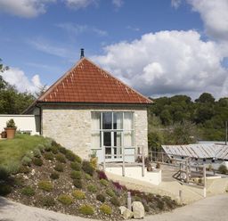 A small stone building with a red tiled roof and garden on a slope at Leys At Valley View Farm in Uplyme