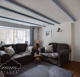 A sitting room with two grey sofas a small wooden table with cups and snacks and blue patterned curtains at Lilac Cottage in Burton Bradstock