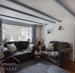 A living room with two sofas a window with patterned curtains and a view of an adjoining kitchen at Lilac Cottage in Burton Bradstock
