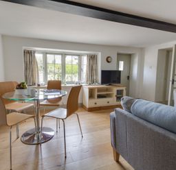 A living room with a glass dining table and wooden chairs a television on a wooden cabinet and a sofa at Little Forge in West Lulworth