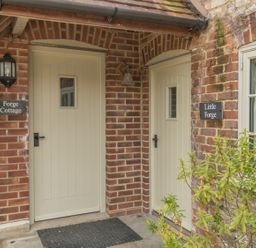 Two cream doors with small windows set in a brick wall with signs reading Forge Cottage and Little Forge at Little Forge in West Lulworth