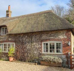 A stone cottage with a thatched roof and a wooden gate at Little Forge in West Lulworth